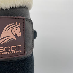 Eine braune Gamasche mit Teddyfellrand und drei Klettverschlüssen von der Marke Ascot Reitsportartikel. Logoausschnitt.